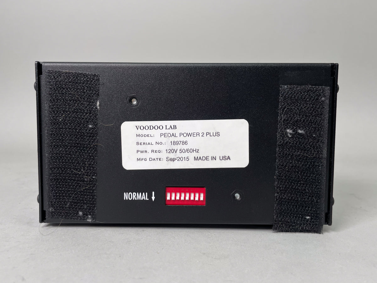 The black pedal power supply is viewed from the back, showing a white label and a row of red DIP switches.