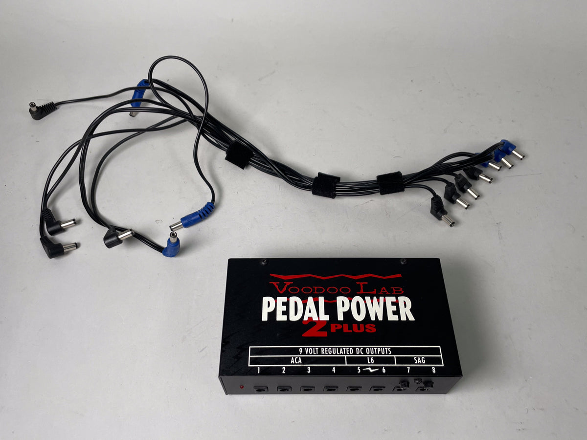Black pedal power supply with red and white lettering, shown with a bundle of black cables with various black and blue connectors.
