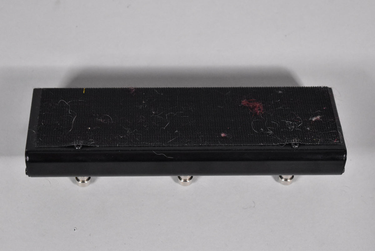 The black pedal's underside is visible, showing three silver feet and a textured, lint-covered top surface with red and yellow marks.