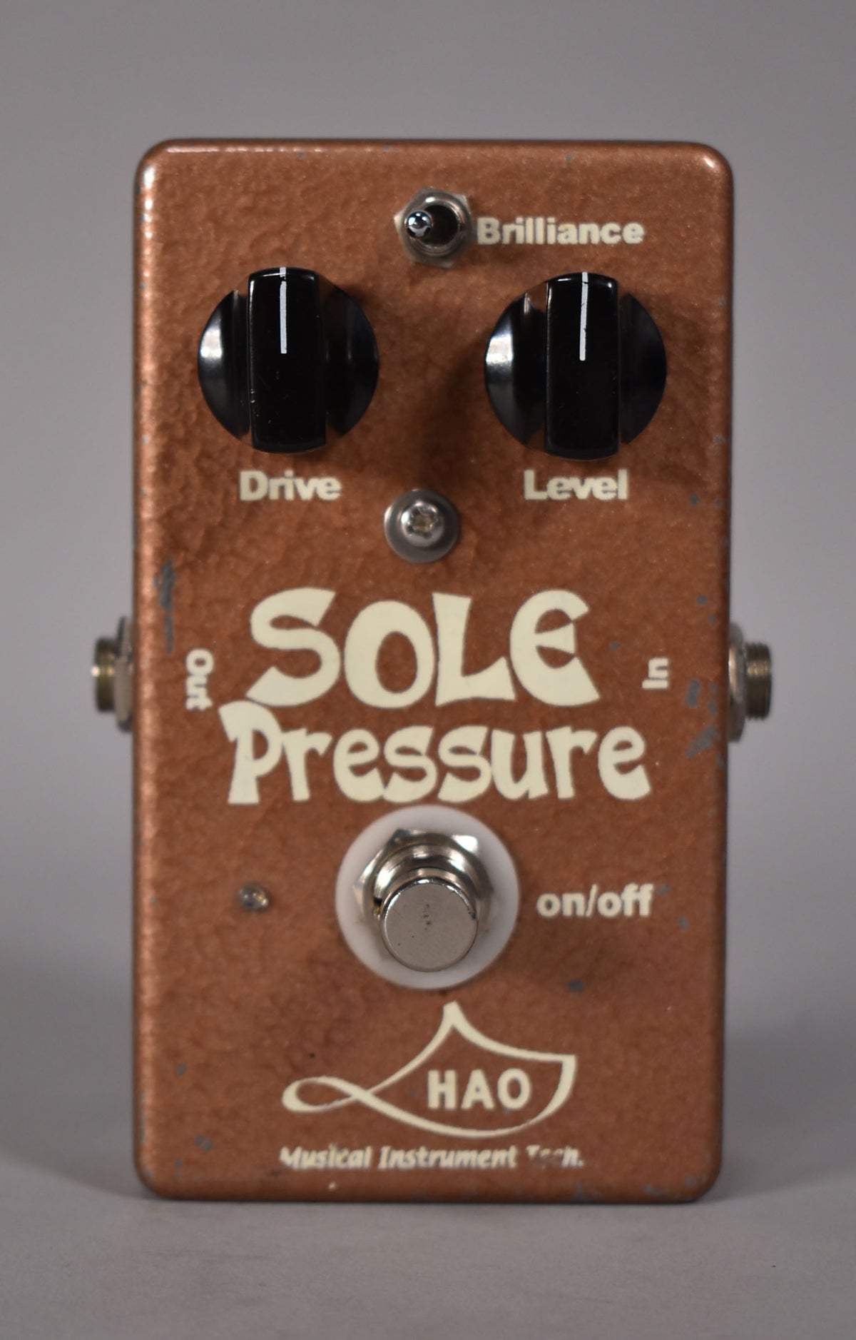Full frontal view of a copper-colored pedal with a textured finish, three black knobs, a toggle switch, and a footswitch.
