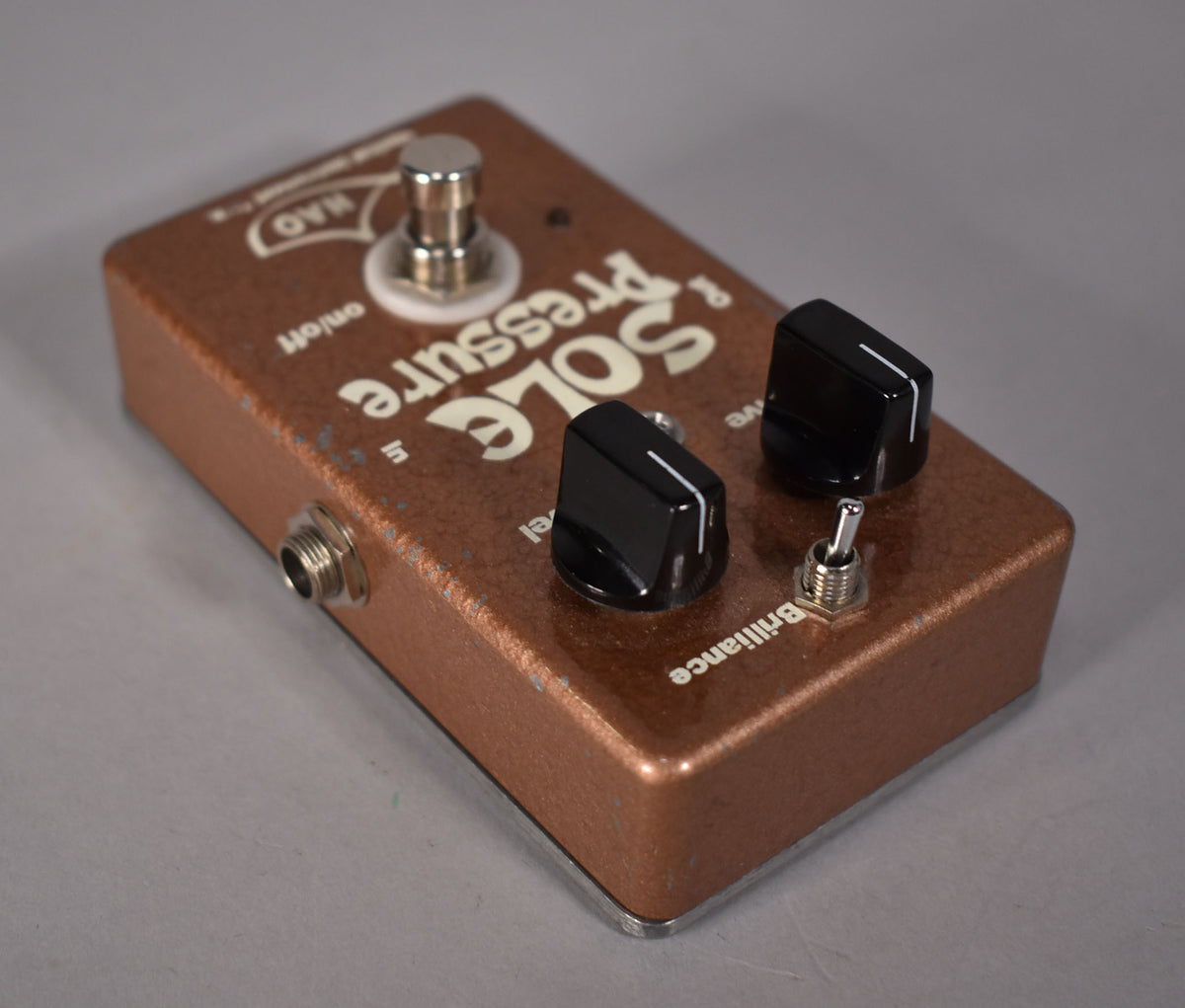 A copper-colored pedal with a textured finish, showing two black knobs, a toggle switch, and a footswitch.