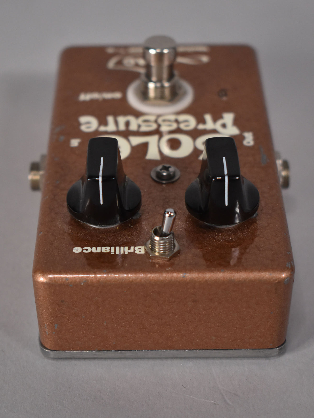 Copper-sparkle pedal, angled from above, showing two black knobs with white lines, a metal toggle switch, and a footswitch.