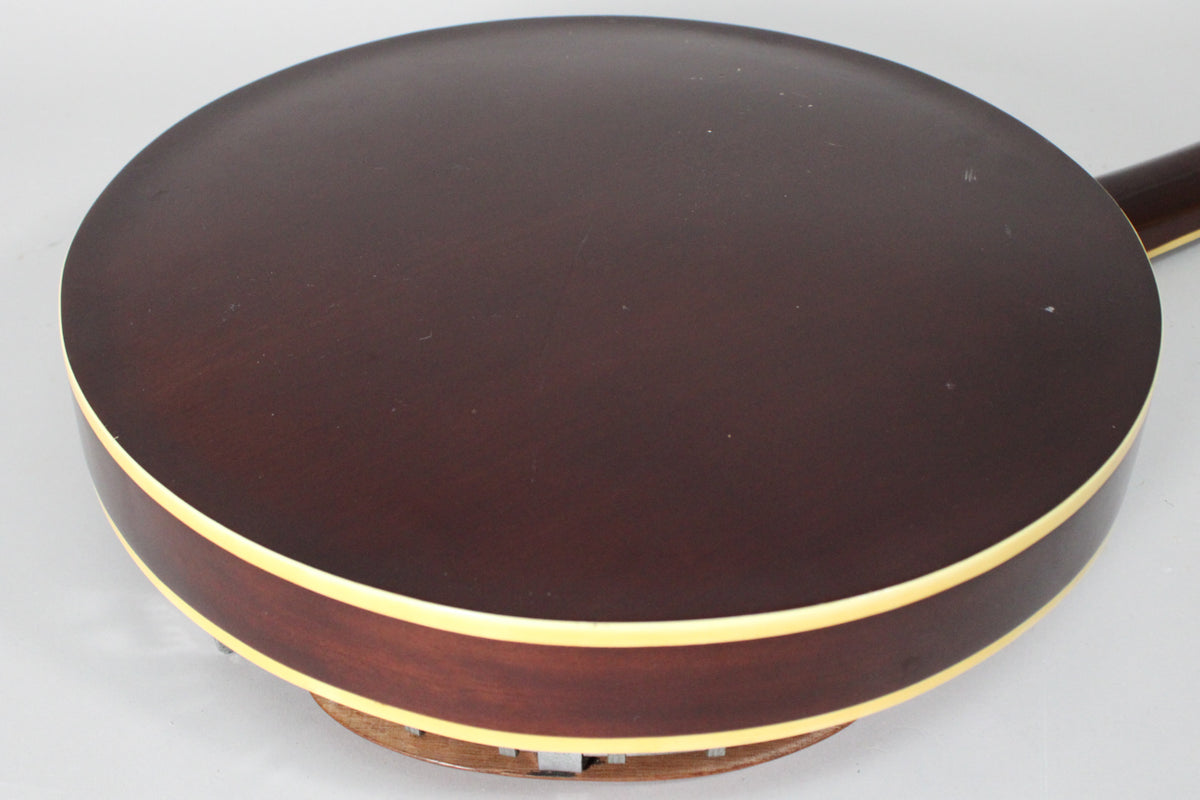 The banjo's dark brown resonator back and sides are visible, with cream binding and light wear, from a high angle.