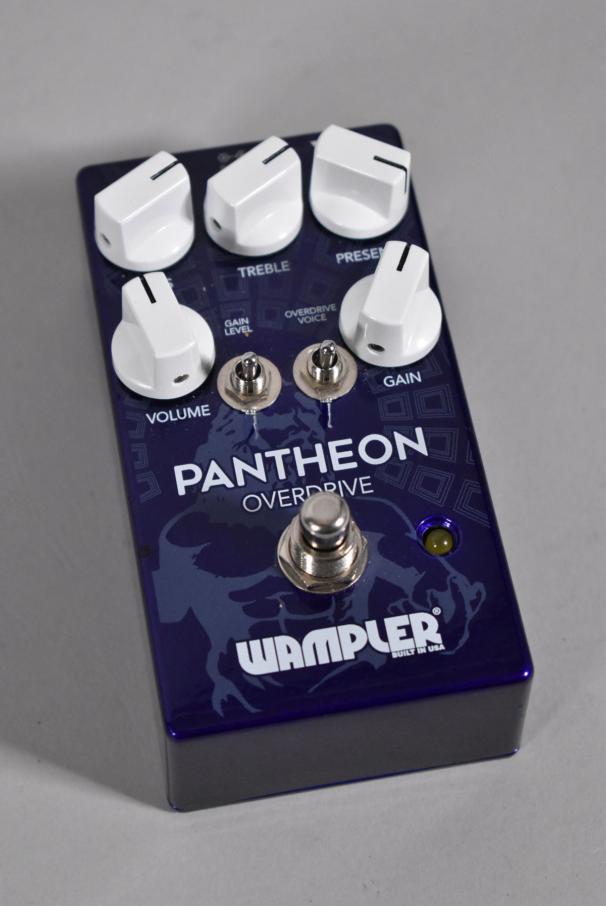 A dark purple effects pedal, angled from above, with five white control knobs, two mini-toggle switches, and a footswitch.