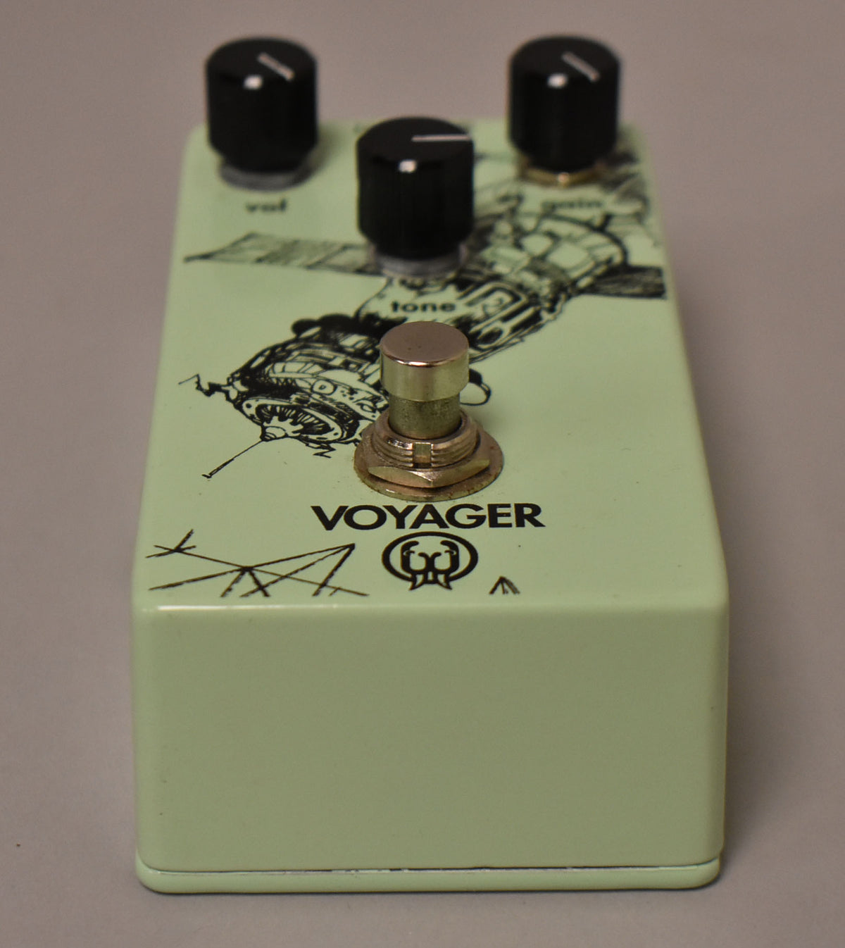 A light green effect pedal with a black line art drawing of a spaceship, three black knobs, and a brass footswitch.