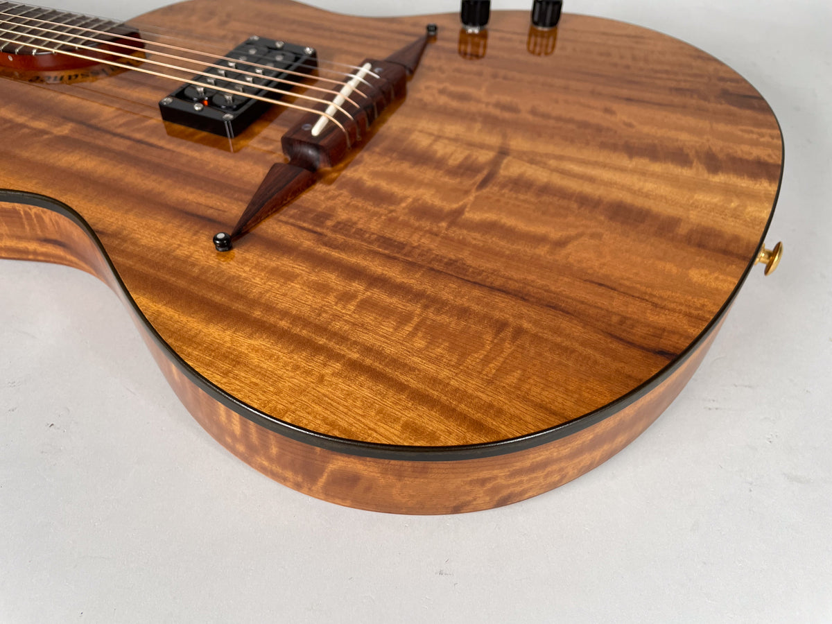 Close-up of the guitar's lower bout, showing the figured koa top and sides, black binding, and a dark wood tailpiece with white string pins.
