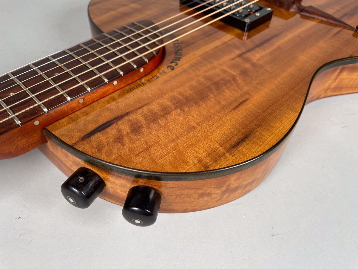 Close-up of the guitar's lower bout, showing the figured koa top, dark binding, and two black control knobs on the side.