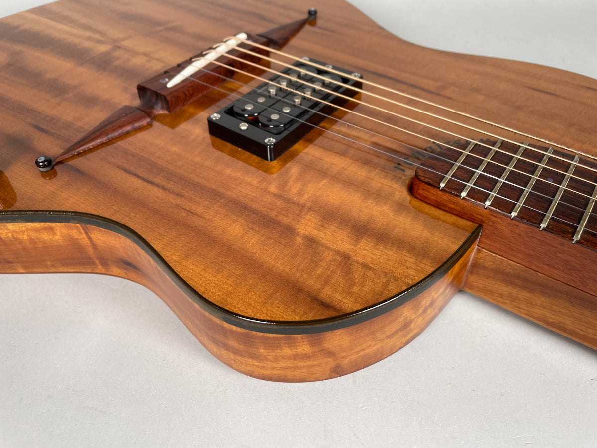 Close-up of the guitar's lower bout, showing the glossy, figured koa body, black pickup, and part of the fretboard.