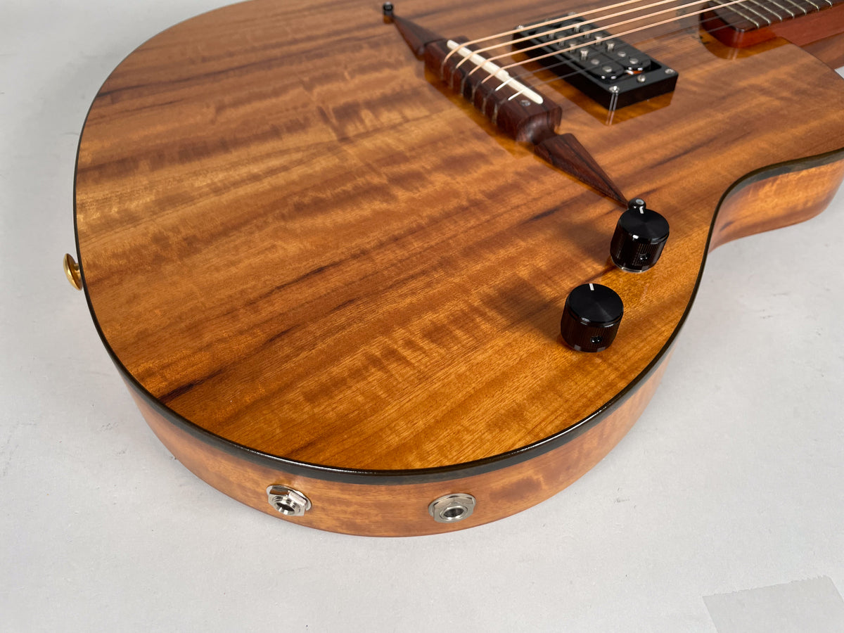 Close-up of the guitar's lower bout, showing the figured koa top, two black control knobs, and two output jacks on the side.