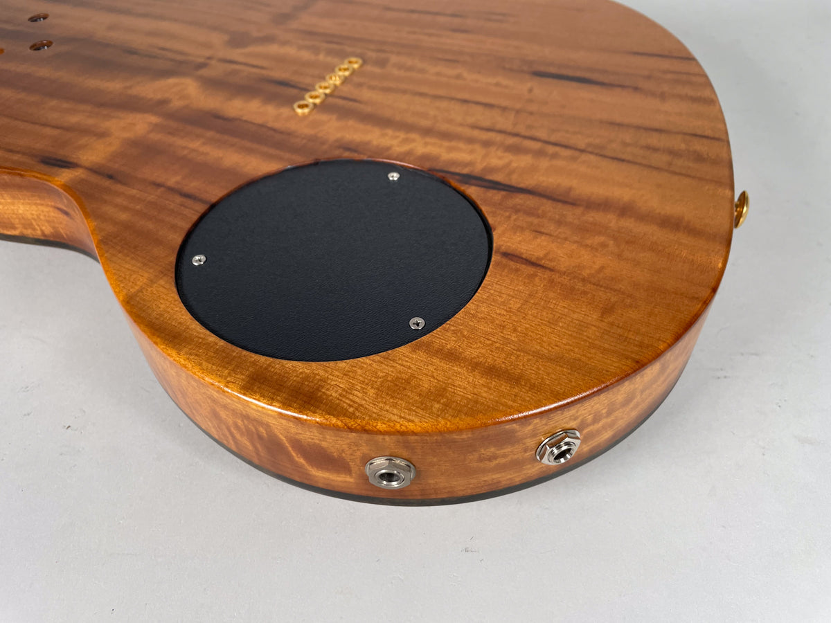 The guitar's koa back shows a black circular control plate and two chrome output jacks on the lower bout.