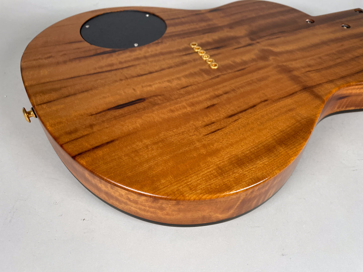 The guitar's glossy koa back, with dark streaks and flame figuring, shows a black control plate and gold string ferrules.