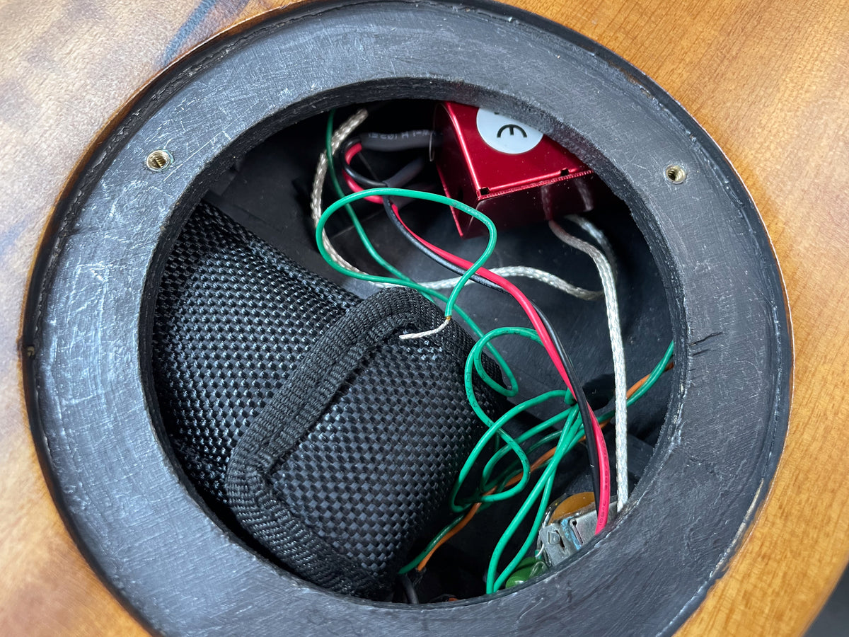 Close-up of the guitar's soundhole, revealing internal wiring, a red component, and a black fabric pouch.