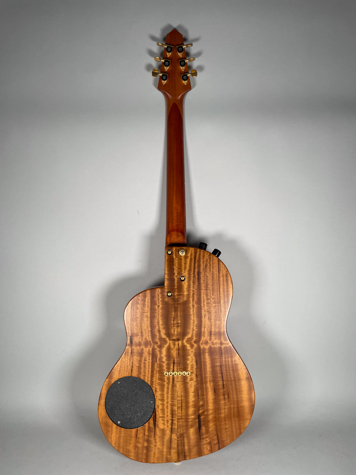 The guitar's koa back shows prominent figuring, with gold tuners and bridge, and a black circular access panel.