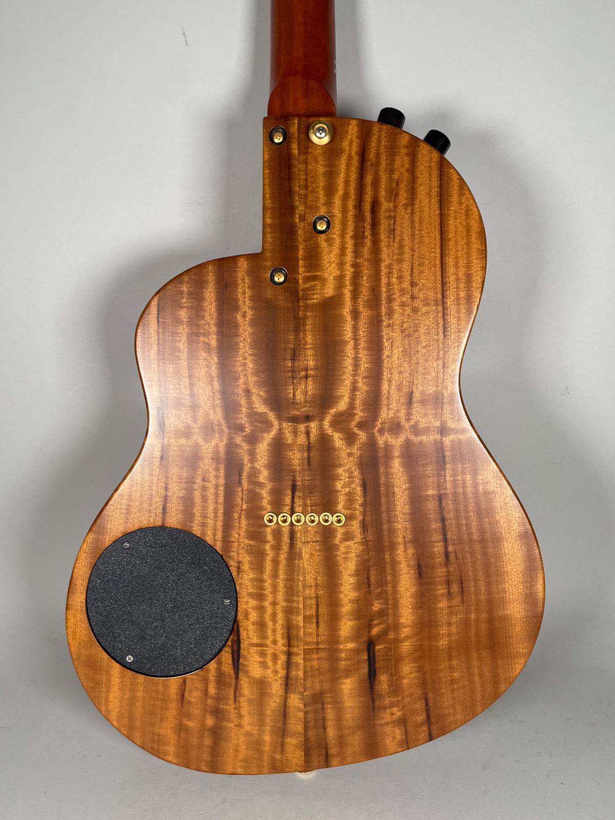 The guitar's back shows a figured koa wood grain, a black circular control plate, and six gold string ferrules.