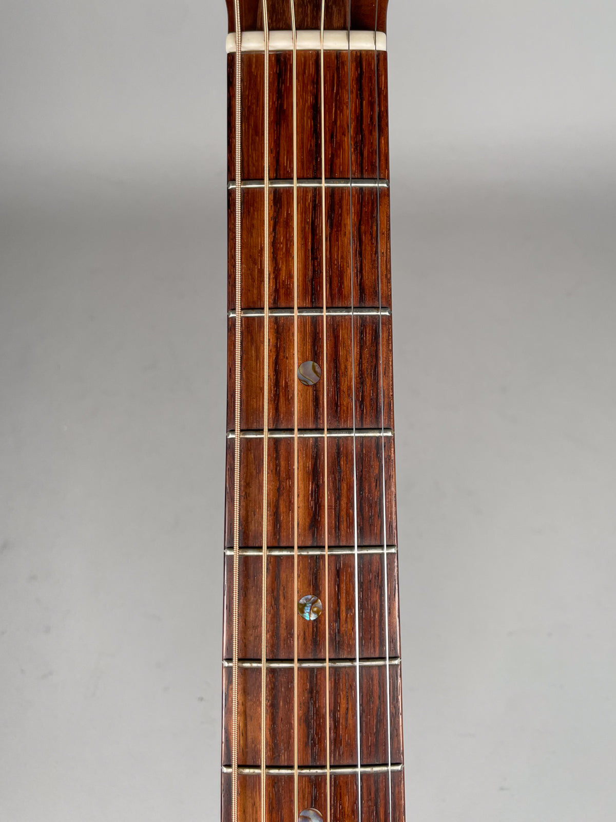 Close-up of the guitar's dark brown fretboard with light wood grain, showing the nut, frets 1-9, and round abalone inlays.