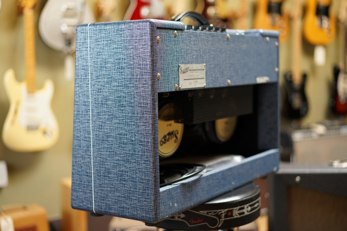 The blue tweed amp is angled right, revealing its back panel, two gold speakers, and a silver control plate.