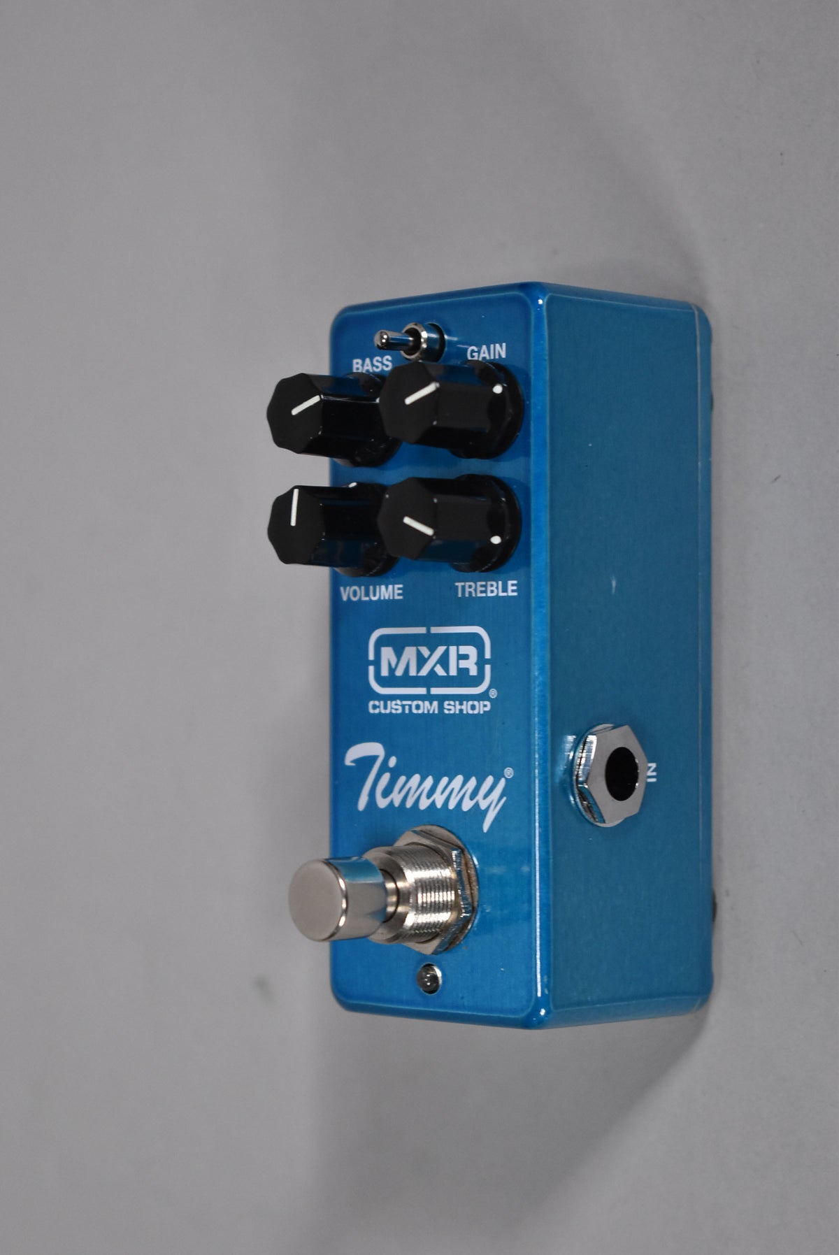 A blue pedal, angled to show the top and right side, with four black knobs, a toggle switch, and a footswitch.