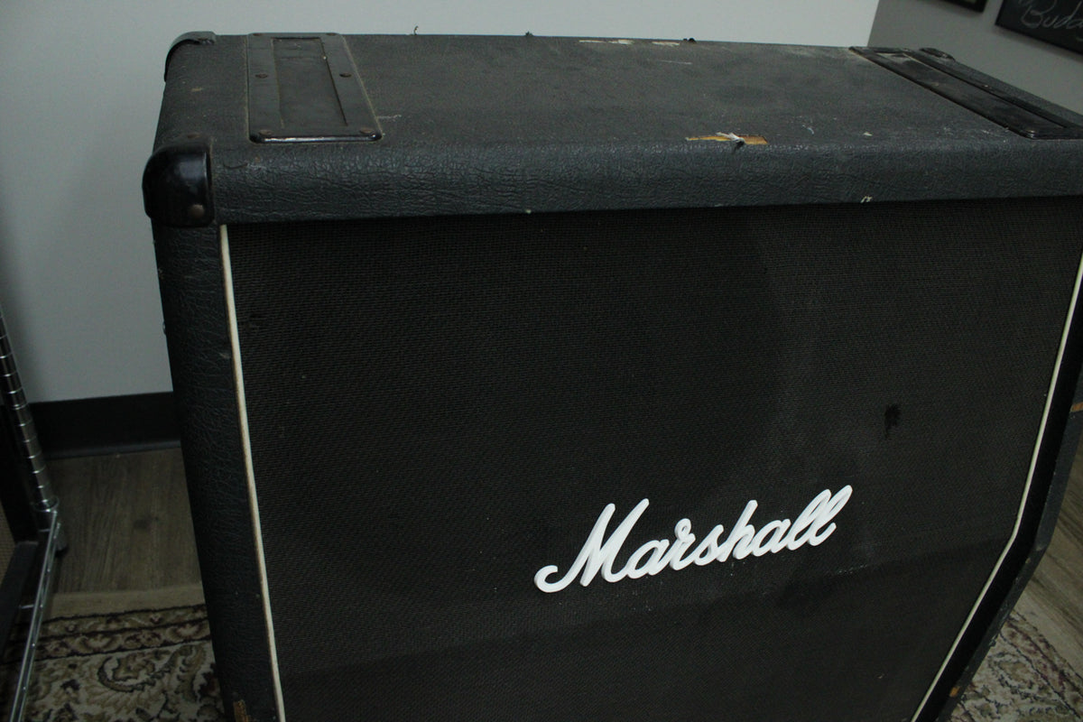 Black textured cabinet, angled from the top left, showing the front grille with white piping and a white script logo, plus a worn top handle.