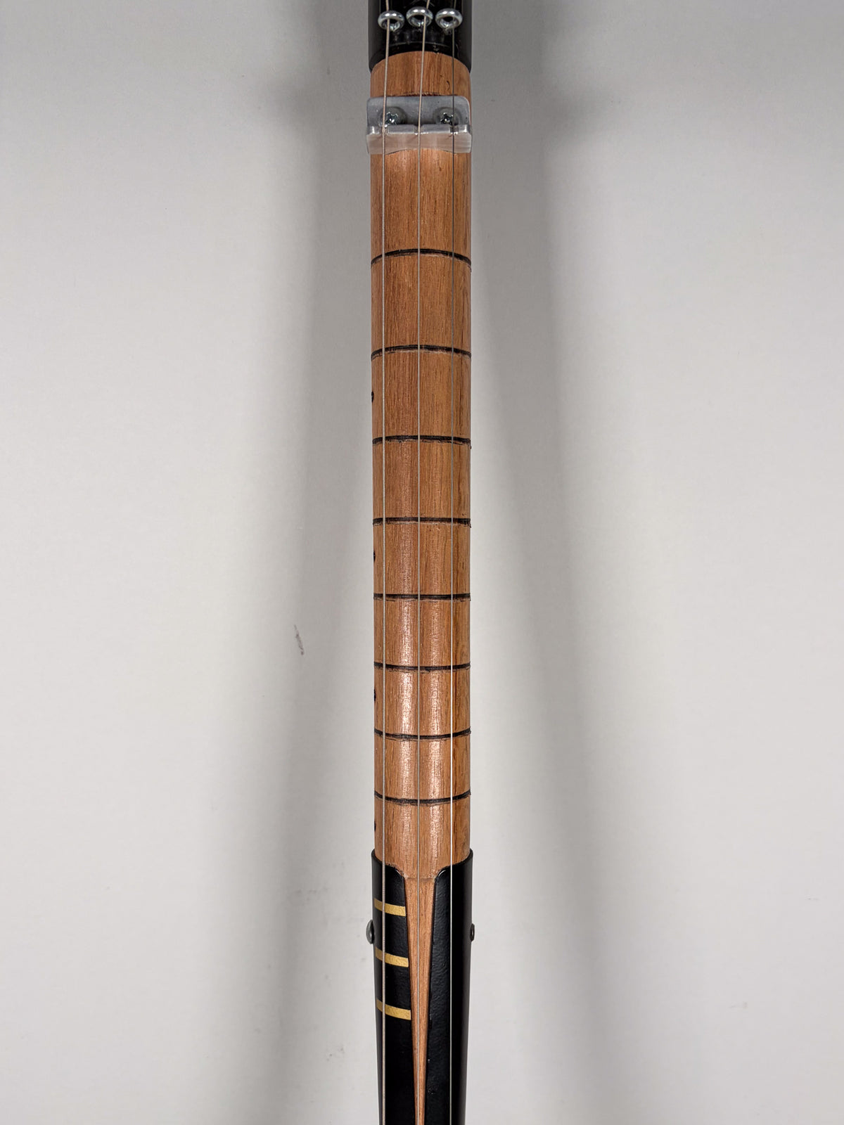 The shovel guitar's light wood fretboard with dark fret lines is centered, framed by a black body with gold stripes at the bottom.