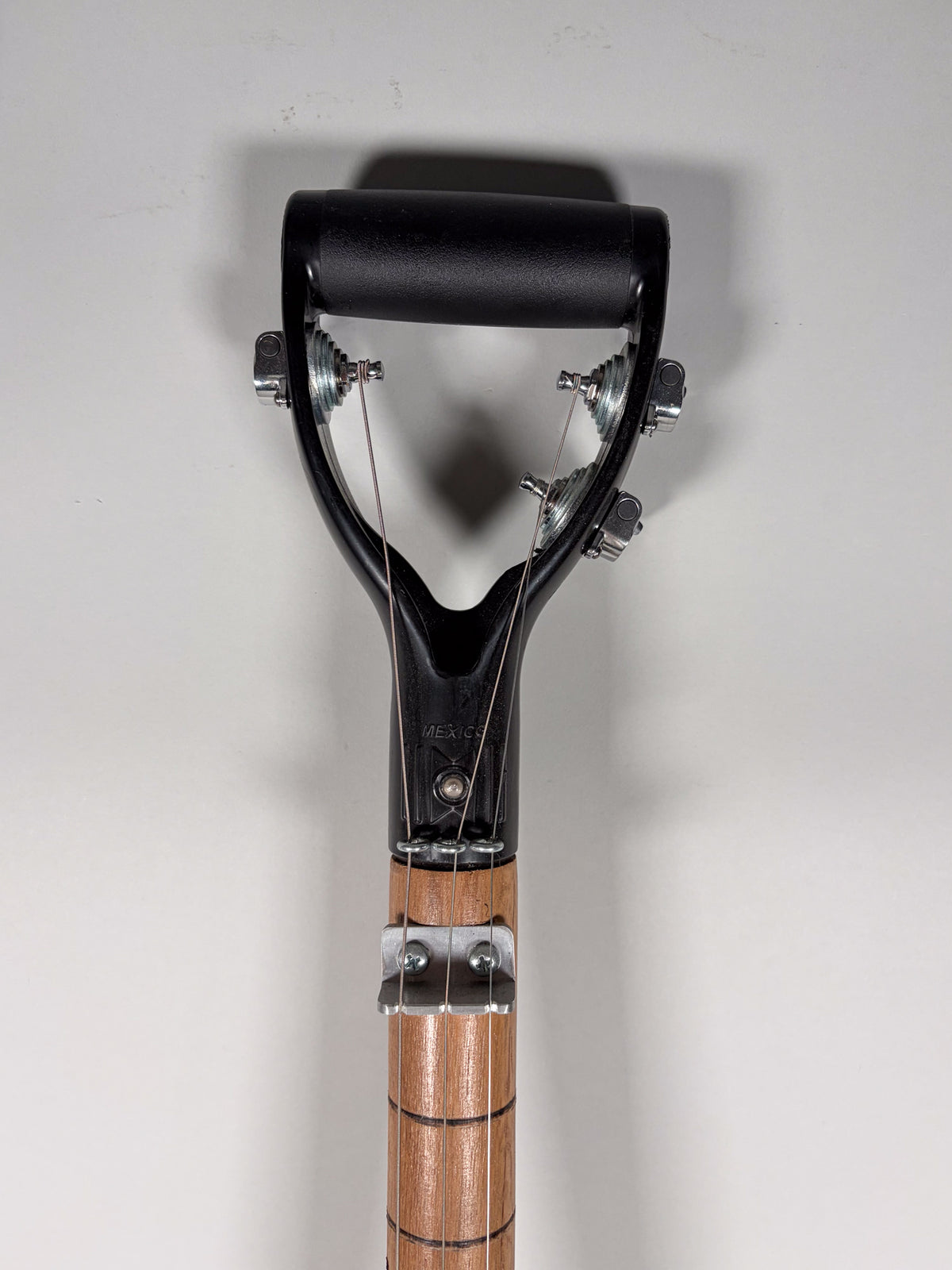 The shovel guitar's black plastic D-handle headstock with four chrome tuners is visible, attached to a light brown wooden neck.