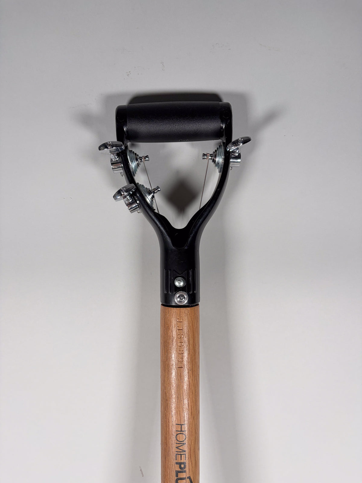 The shovel guitar is viewed from above, showing the black D-handle with three chrome tuners and strings, attached to a light wood shaft.