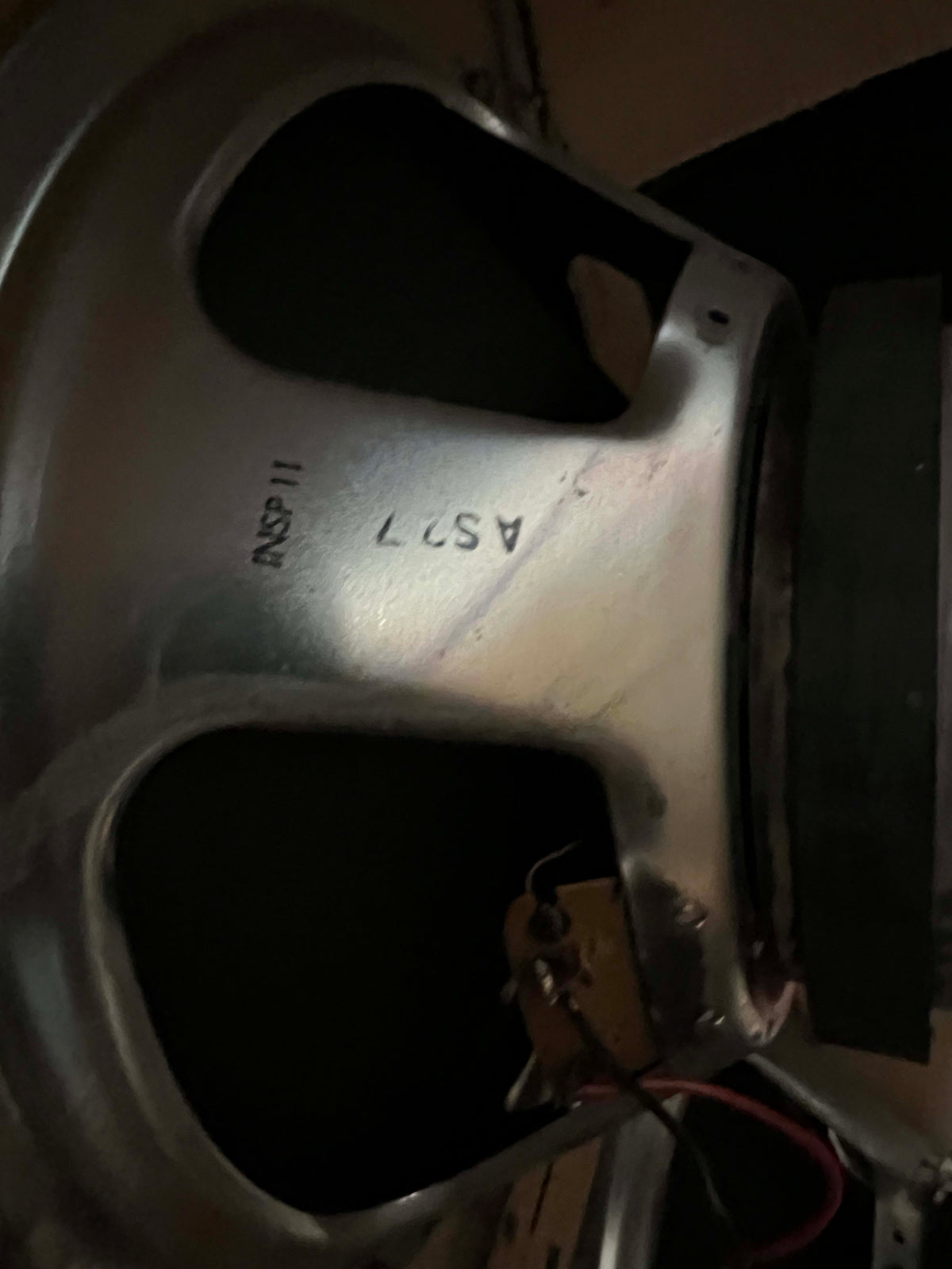 Close-up of a silver speaker frame with "AS27" and "INSP 11" stamped, showing wiring and a yellow capacitor.
