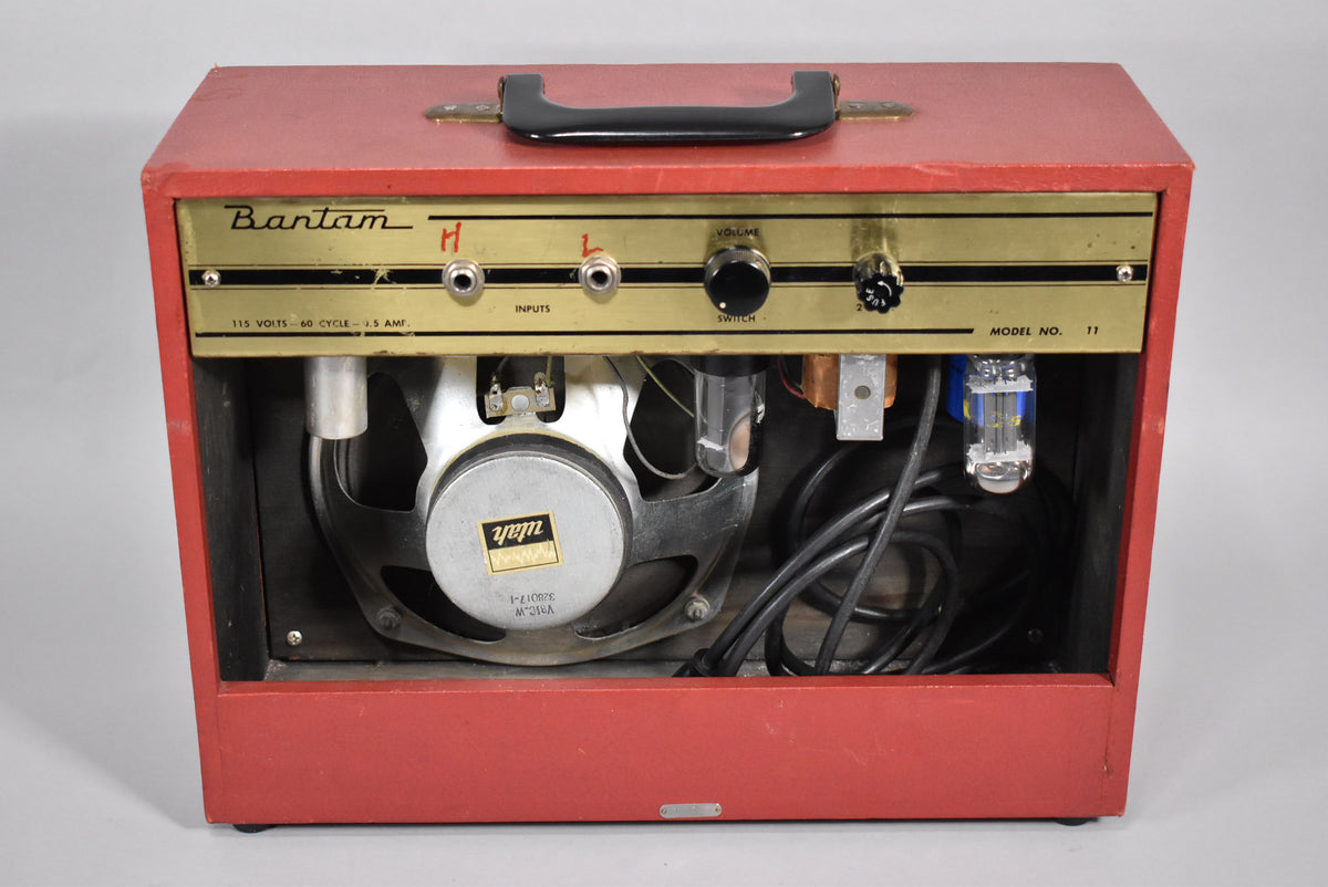 Rear view of a red combo amp with a gold control panel, showing the speaker, tubes, and wiring inside the open back.