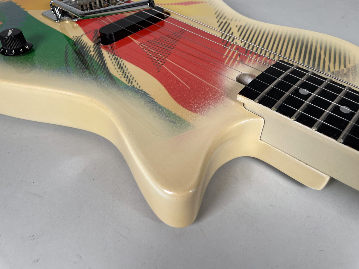 Close-up of the guitar's lower body, showing the cream finish with red, green, and black graphic, a single black pickup, and volume knob.