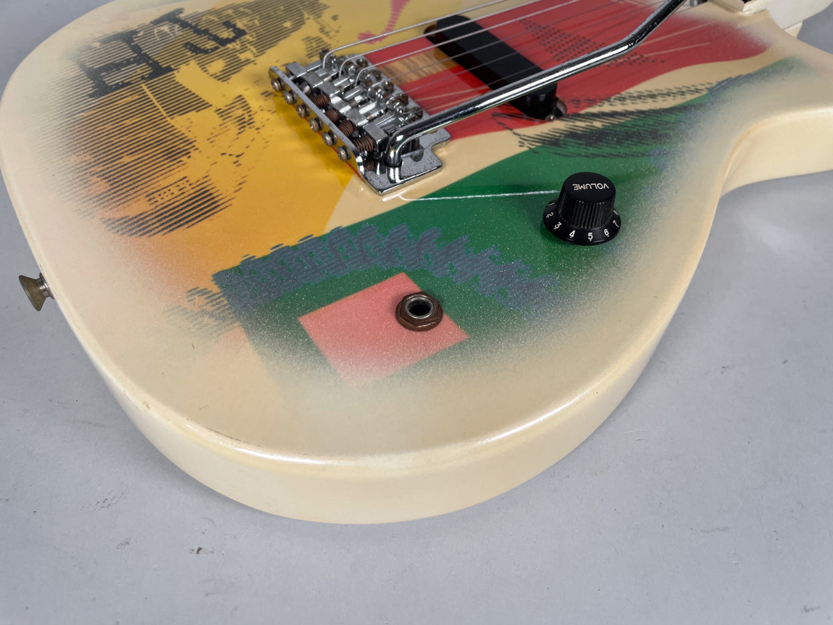 Close-up of the guitar's lower body, showing the vibrato bridge, black volume knob, and colorful graphic design on the cream finish.