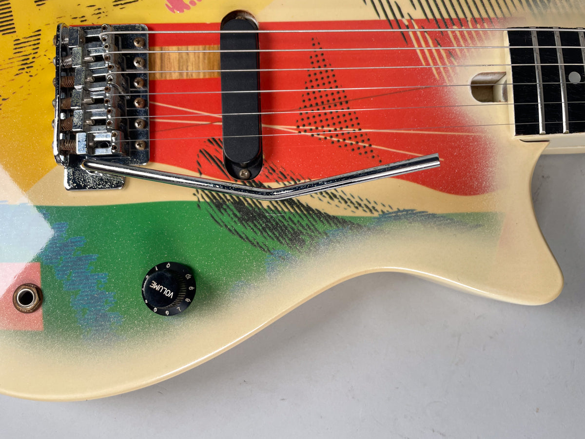 Close-up of the lower body, showing the colorful graphic finish, chrome tremolo bridge, single black pickup, and volume knob.