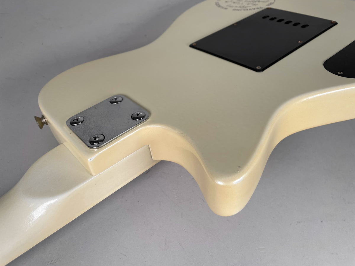 The back of the cream-colored electric guitar body, showing the neck plate, strap button, and two black control cavity covers.