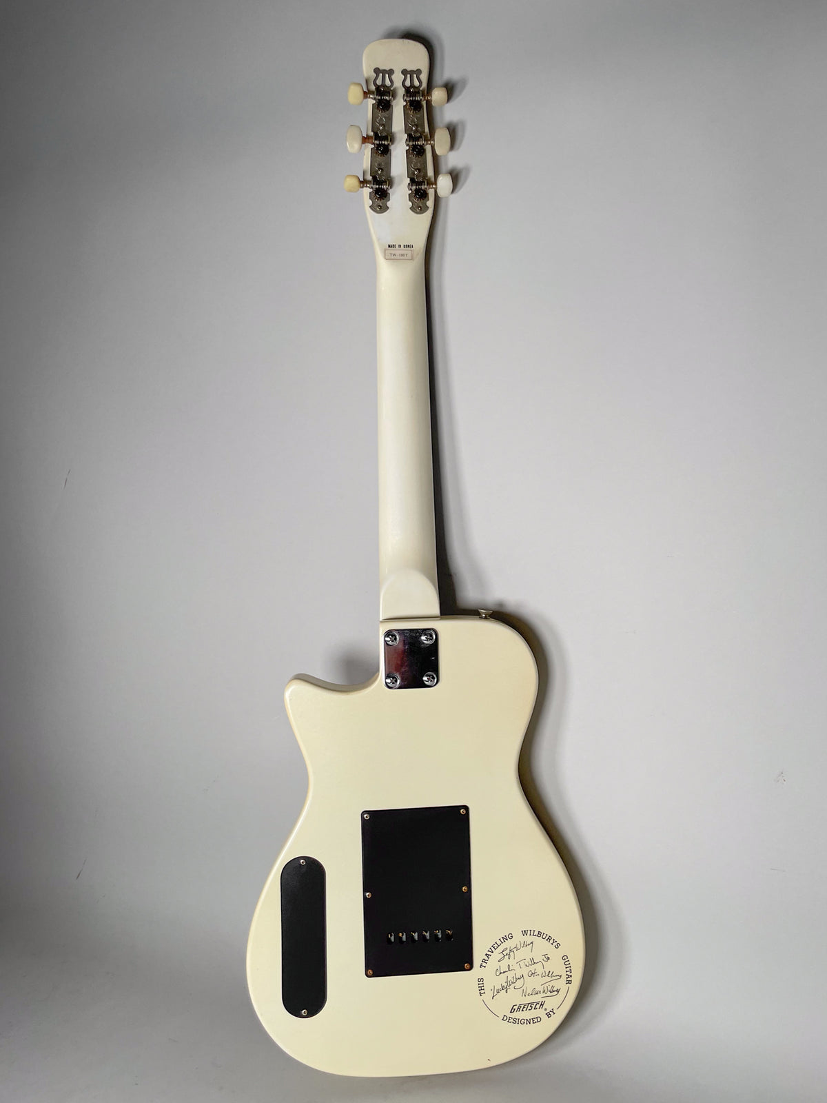 Rear view of a cream-colored electric guitar, showing the neck, headstock with six tuners, and body with a black control plate.