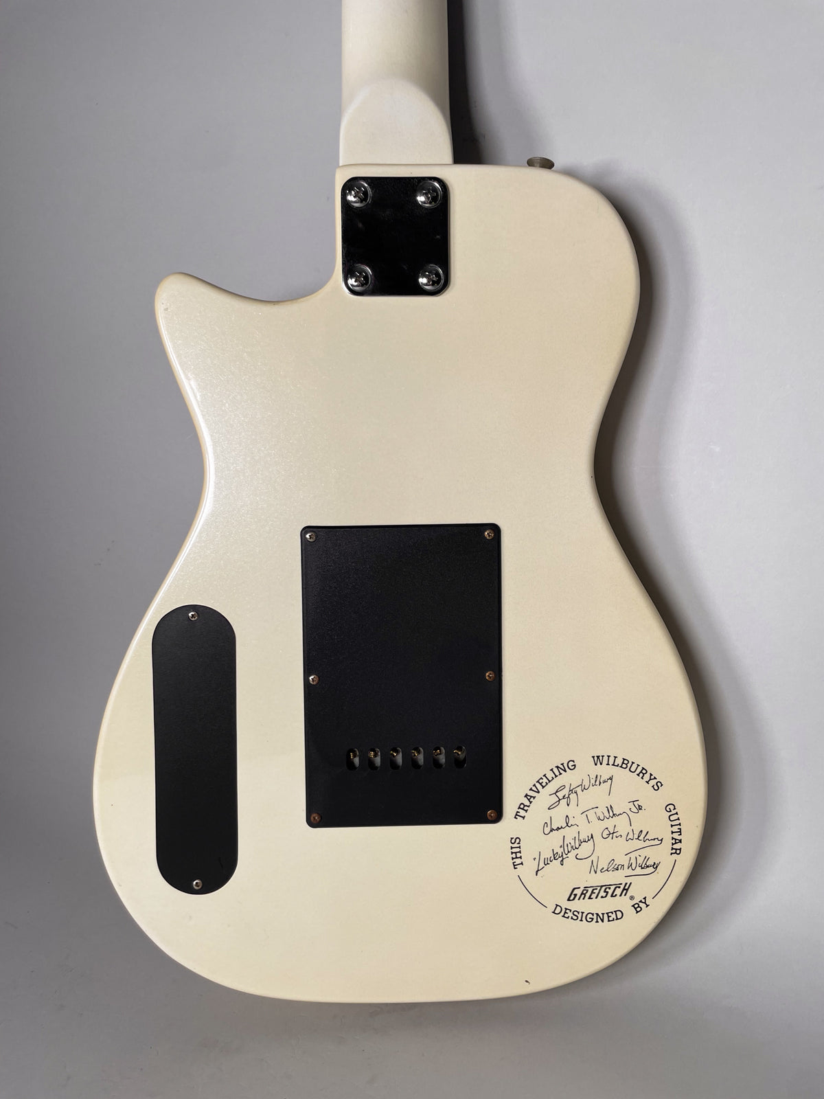 Rear view of a cream-colored electric guitar body with a black neck plate, two black control cavity covers, and a faint circular graphic.