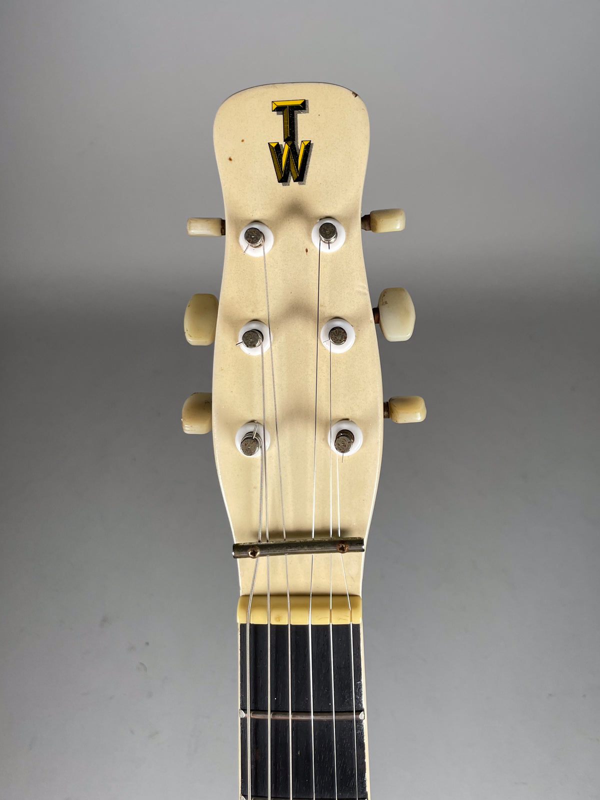 Close-up of the guitar's cream-colored headstock, showing six tuning pegs, a dark "TW" logo, and some minor finish wear.