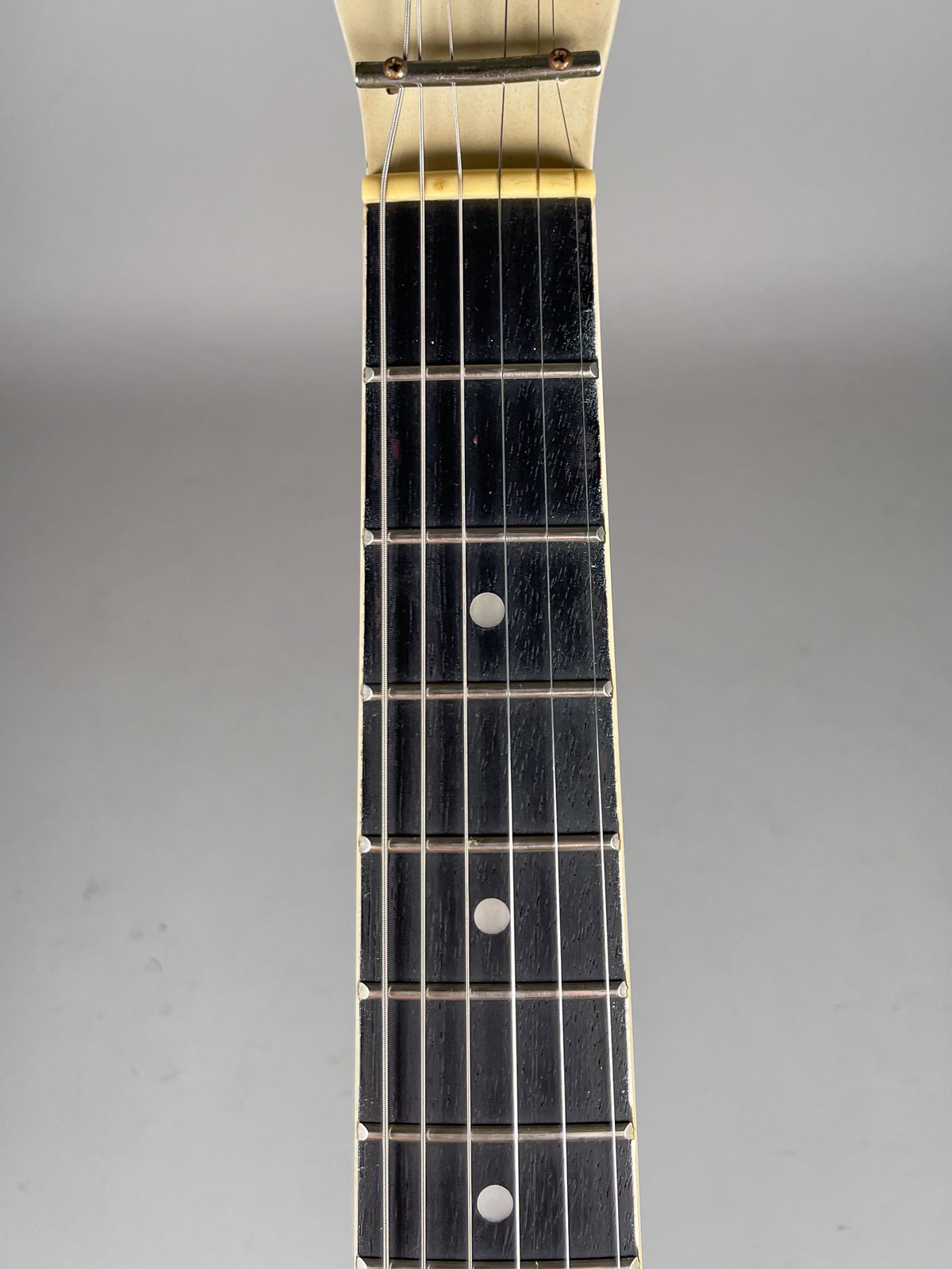 Close-up of the guitar's dark fretboard with white dot inlays, showing light wear and a cream-colored nut and headstock.