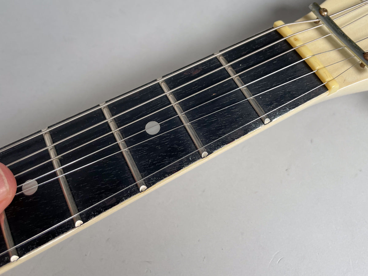 Close-up of the dark fretboard with light fret markers, showing some wear and a cream-colored nut at the top.