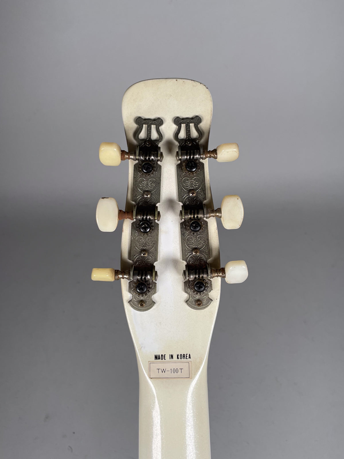 Rear view of the guitar's cream headstock and neck, showing six cream tuning pegs on ornate silver-grey metal plates.