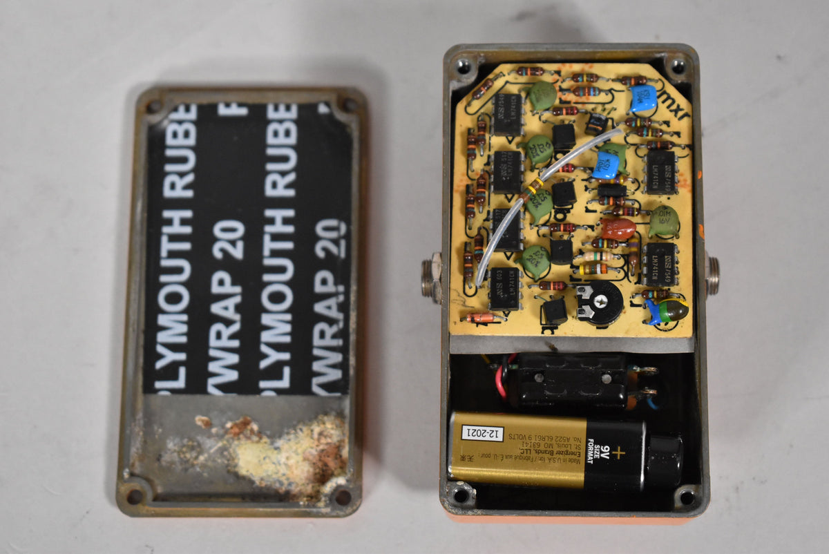 The pedal's orange casing is open, revealing a circuit board with many components and a 9V battery in the lower compartment.