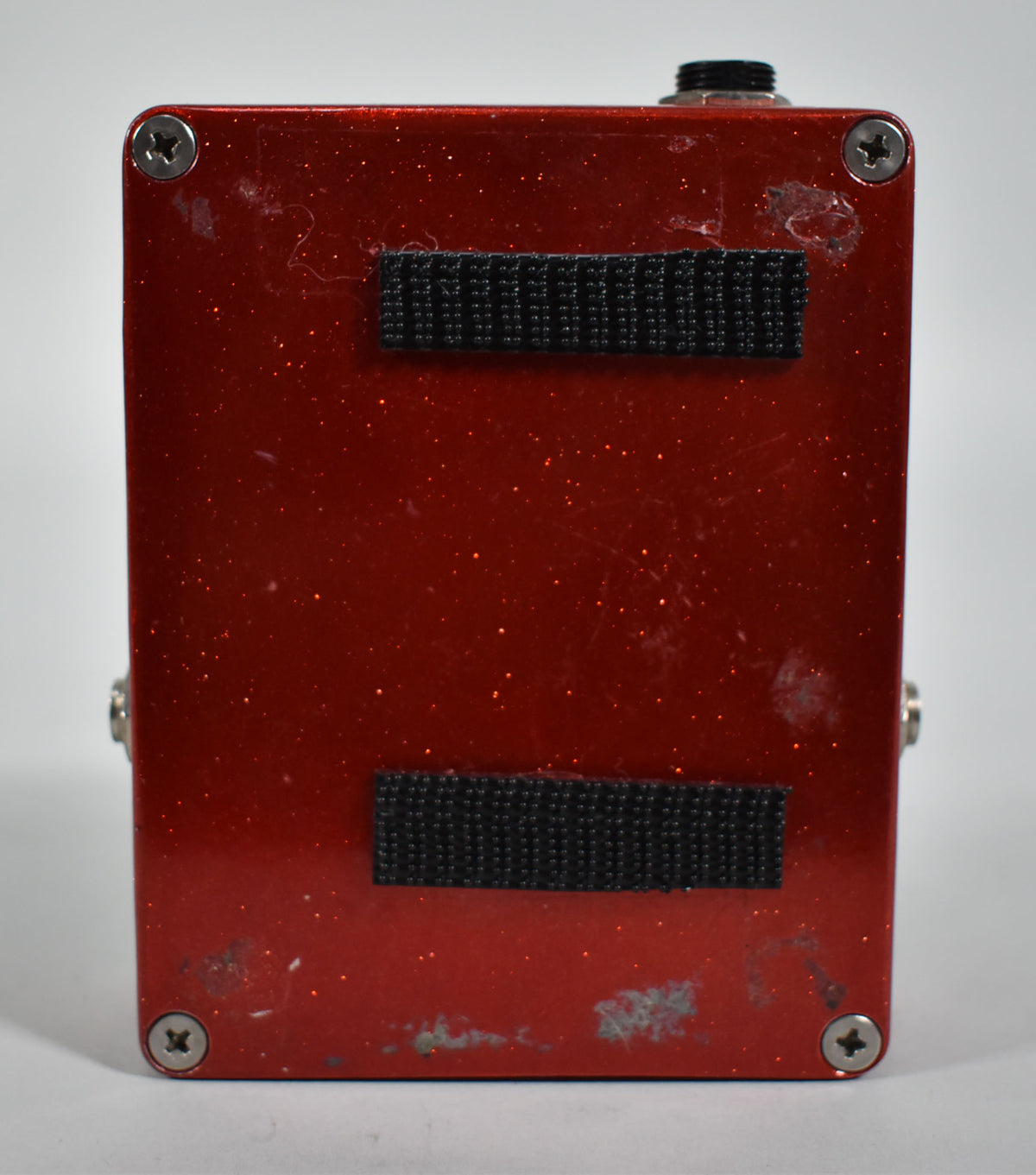 The red sparkle pedal's underside shows two strips of black hook-and-loop tape and scuffs on the finish and screw heads.