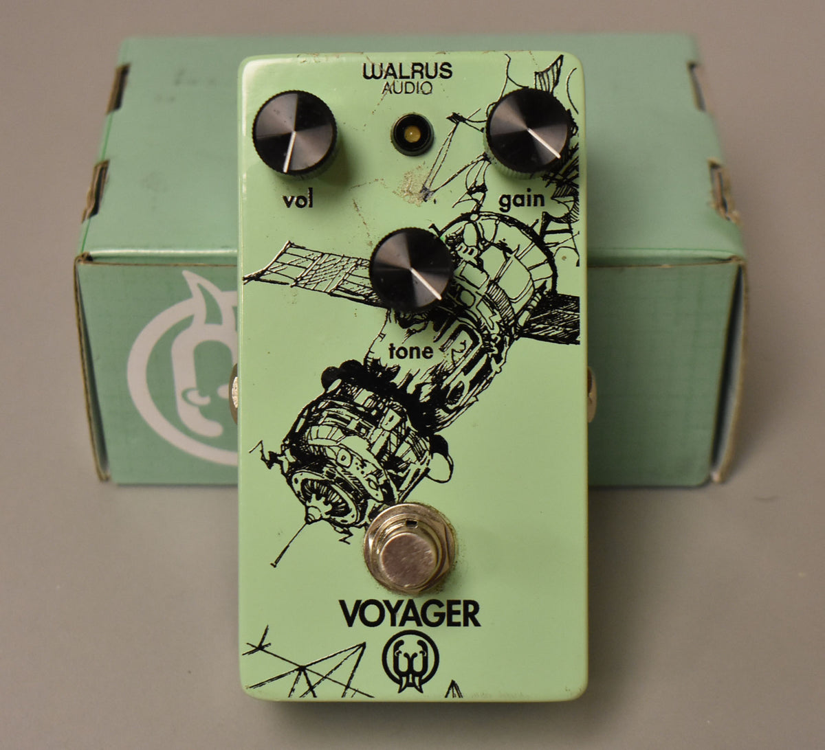 Light green effect pedal with three black knobs labeled "vol," "gain," and "tone," a footswitch, and a satellite graphic.