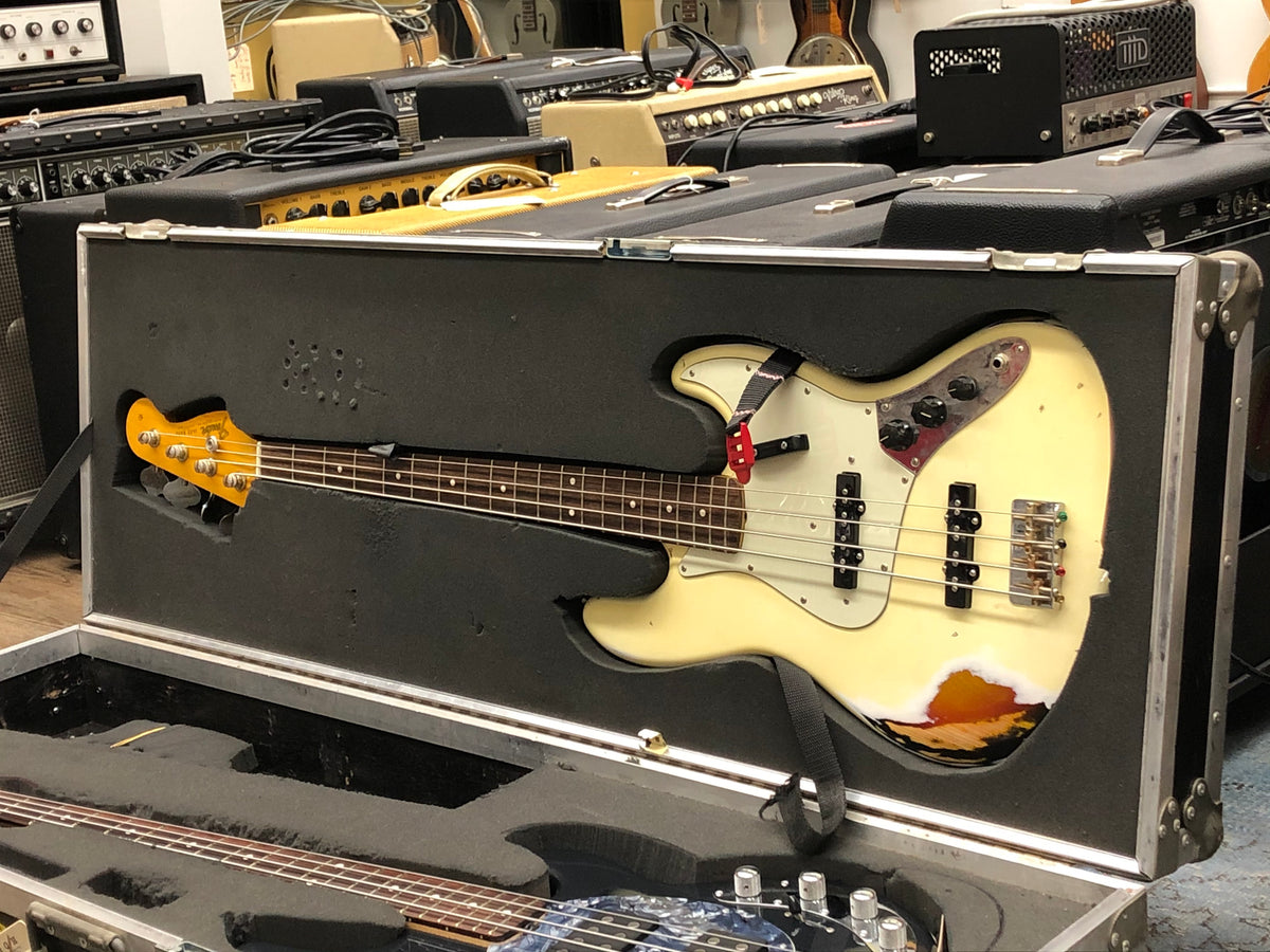 Open black flight case with a cream J-Bass, showing its headstock, neck, and body with heavy wear and exposed wood.
