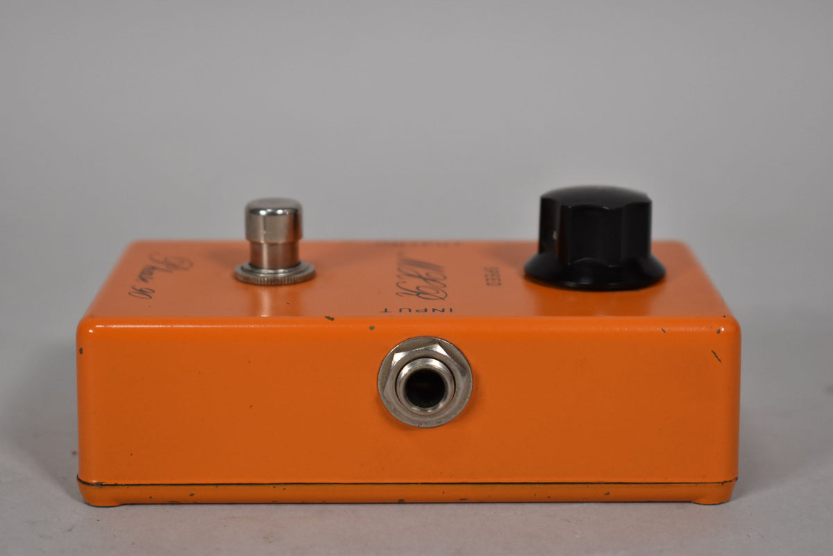 The orange pedal is viewed from the front, showing the input jack, a silver footswitch, and a black speed knob.
