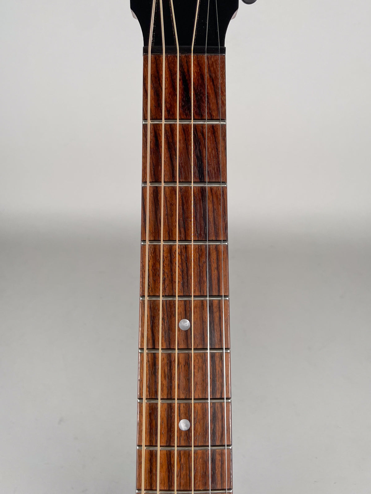 Close-up of the dark brown fretboard with prominent grain, showing the first 12 frets and two white dot inlays.