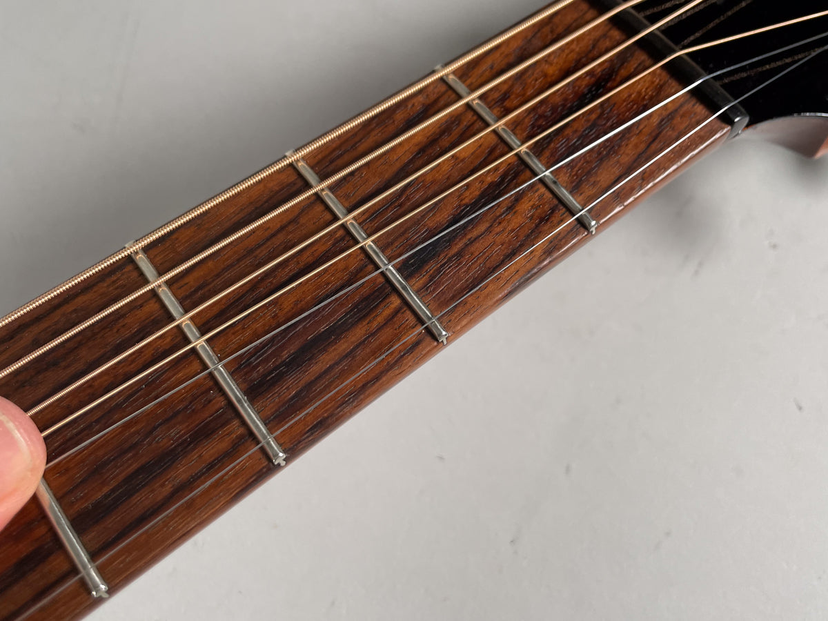 Close-up of the dark brown fretboard with light wood grain, silver frets, and light-colored strings, angled from lower left to upper right.