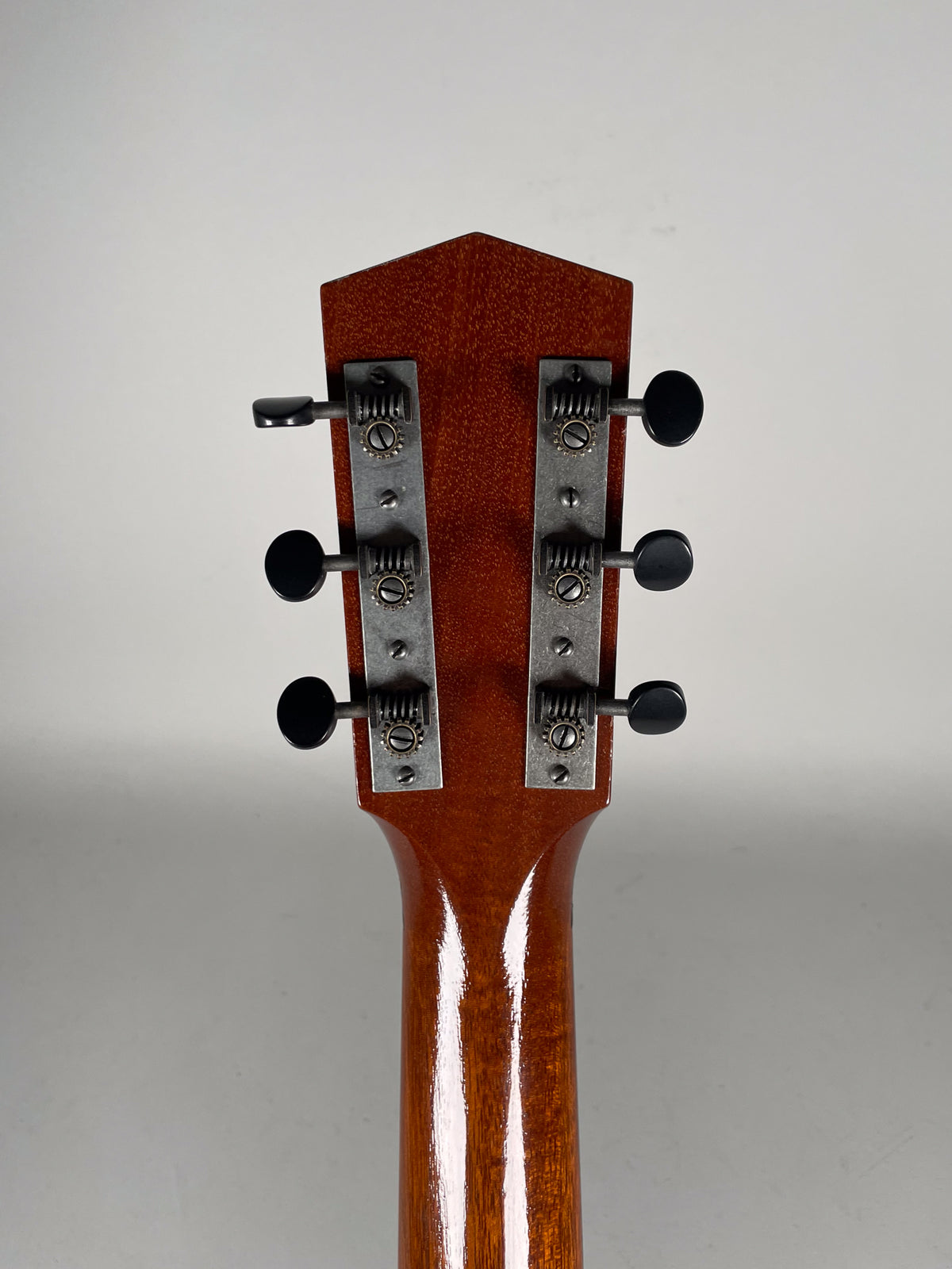The guitar's headstock and upper neck are shown from behind, featuring a glossy brown finish and six open-gear tuners with black buttons.