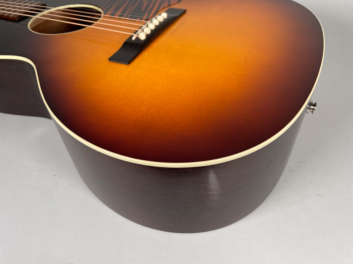 The sunburst acoustic guitar's lower bout and side, showing the dark brown back, cream binding, and endpin jack.