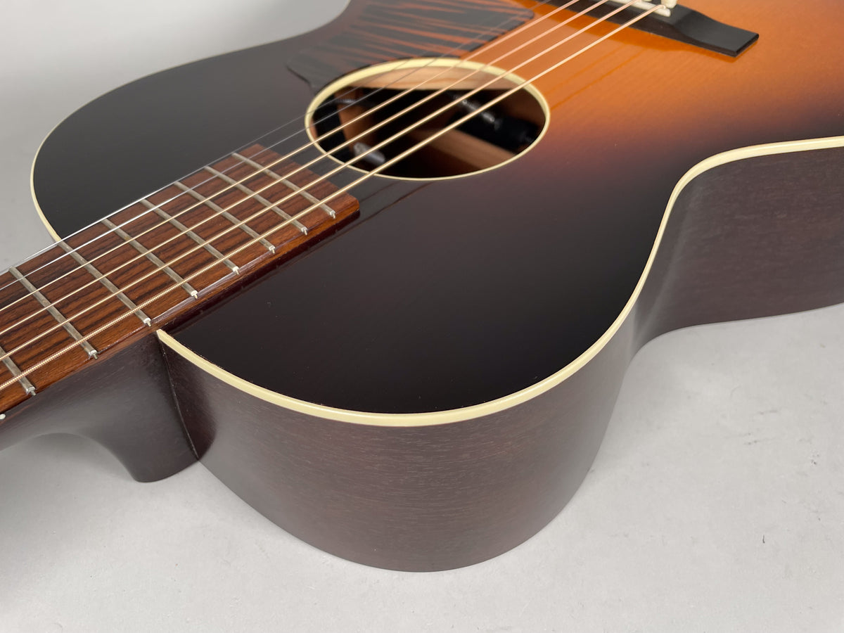 Close-up of the sunburst acoustic guitar's lower bout and fretboard, showing the dark brown back and sides with cream binding.