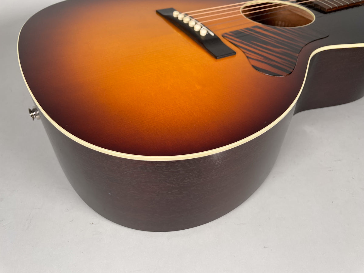 The lower bout of a sunburst acoustic guitar, showing the dark brown sides, cream binding, and endpin jack.