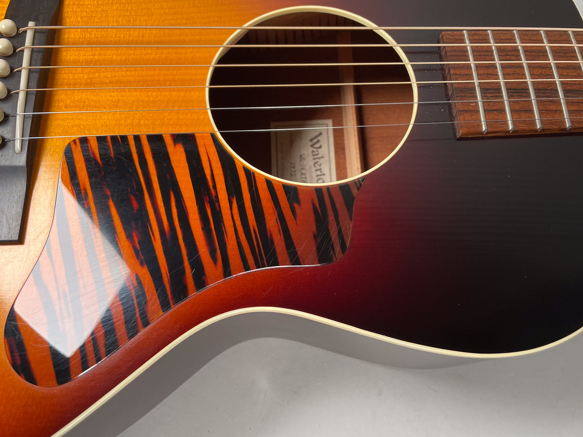 Close-up of the sunburst acoustic guitar body, showing the soundhole, pickguard with scratches, and bridge pins.