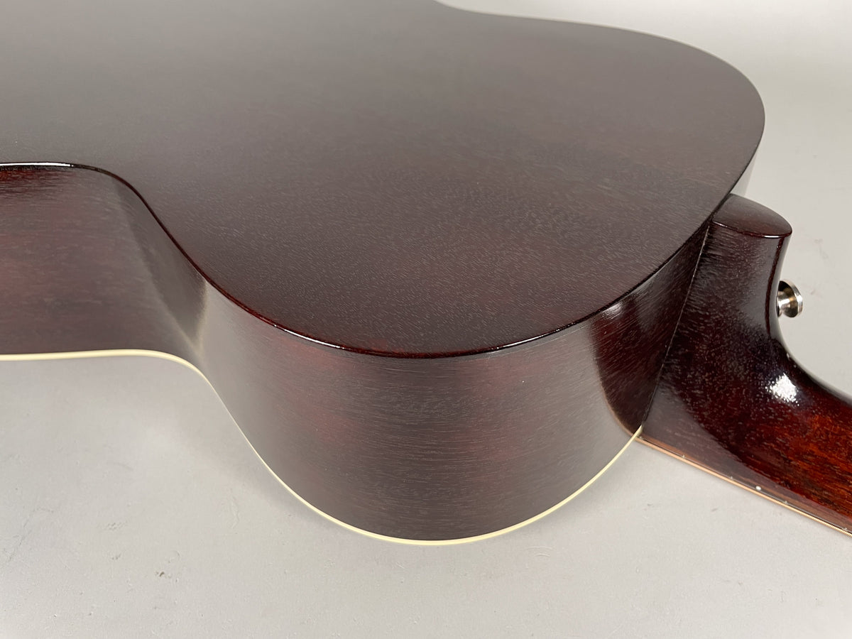 Close-up of the guitar's dark sunburst body and neck heel, showing the cream binding and a chrome endpin jack.
